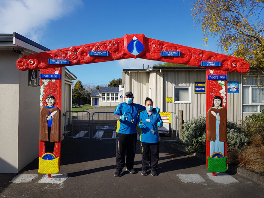 Cleaners standing outside a school giving the thumbs-up.