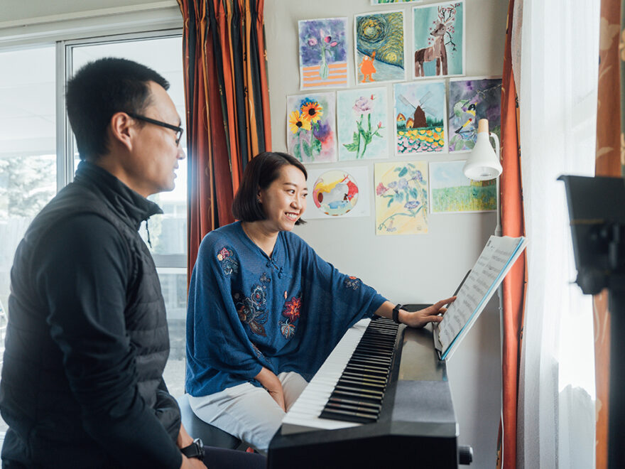 Woman playing the piano with husband sitting next to her.