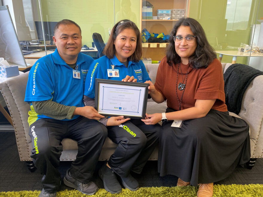 Cleaners sitting on a sofa with framed certificate.